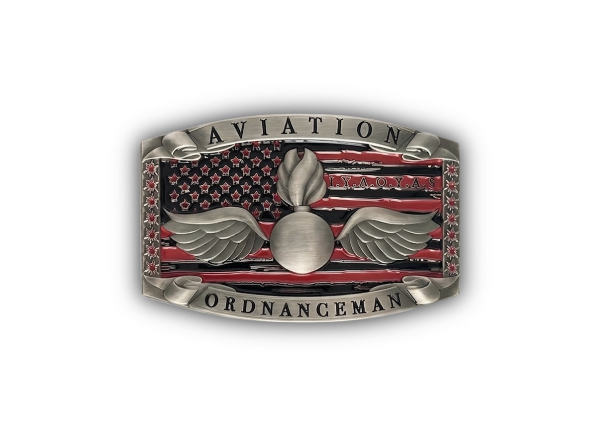 A silver-toned Aviation Ordnance Man belt buckle featuring an American flag design with red and black stripes, a central flame and wing emblem, and the words 'AVIATION' at the top and 'ORDNANCEMAN' at the bottom.