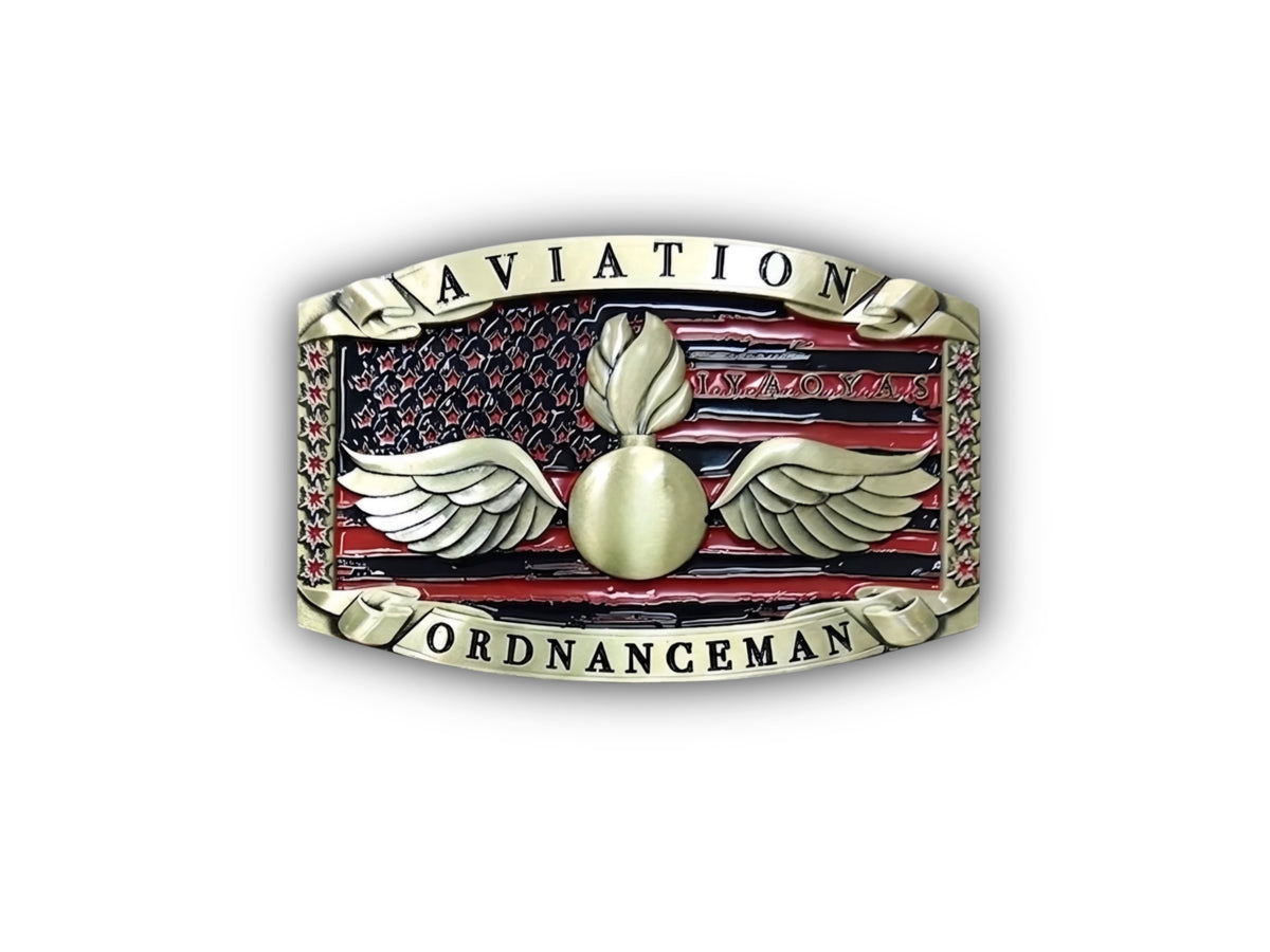 A military-style enamel pin or belt buckle featuring a gold-toned winged grenade emblem on a red and black American flag background, with the words 'AVIATION' at the top and 'ORDNANCEMAN' at the bottom.